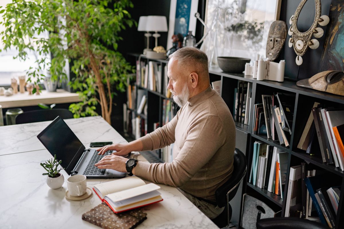 Senior man with gray hair working on a laptop at a home office desk.